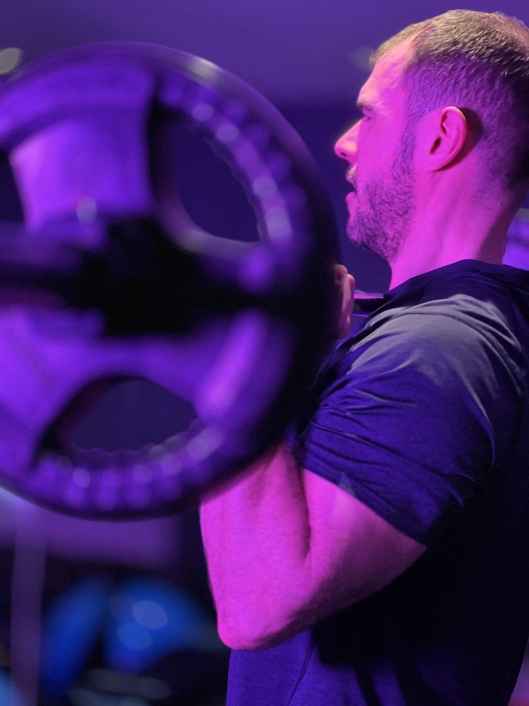 Matthew loading a barbell under violet gym lighting